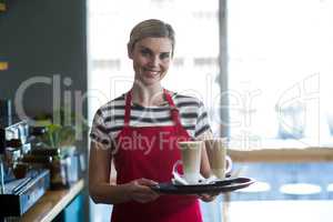 Smiling waitress holding cup of cold coffee at counter in cafe