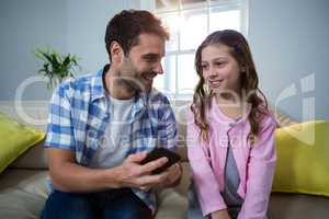 Father holding mobile phone and interacting daughter with in the living room