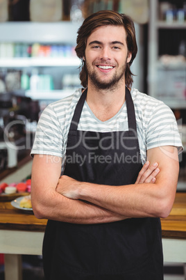 Portrait of smiling waiter standing with arm crossed