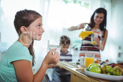 Girl drinking cup of tea with family having breakfast