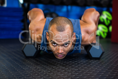 Portrait of serious man doing push-ups with dumbbell