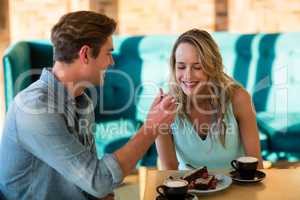 Man feeding cake to woman in cafÃ?Â©