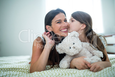 Daughter kissing on mother cheeks on bed