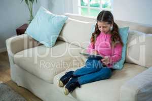 Girl using digital tablet while relaxing on sofa