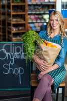 Smiling woman with grocery bag sitting in organic shop