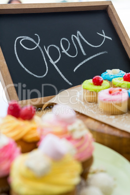 Close-up of various cupcakes on table with open signboard