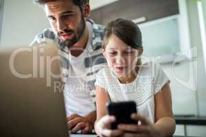 Father and daughter using laptop and mobile phone in the living room