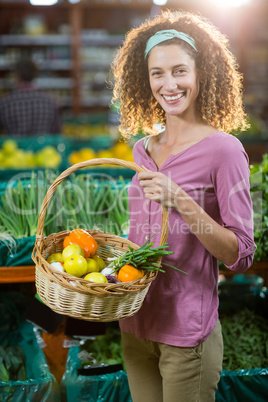 Smiling woman holding basket of vegetables in organic section