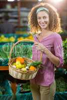 Smiling woman holding basket of vegetables in organic section