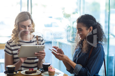 Women using mobile phone and digital tablet while having cup of coffee