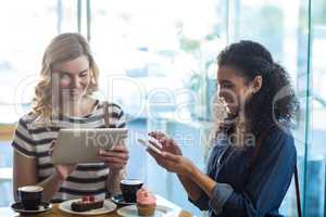 Women using mobile phone and digital tablet while having cup of coffee