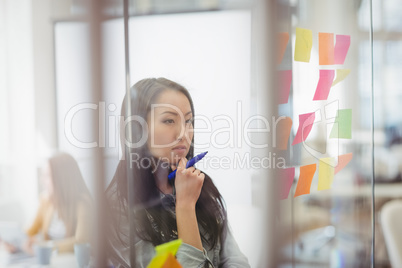 Thoughtful photo editor looking at multi colored sticky notes on glass