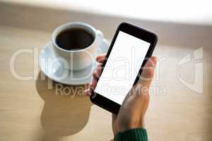 Hand holding mobile phone with cup of coffee in table