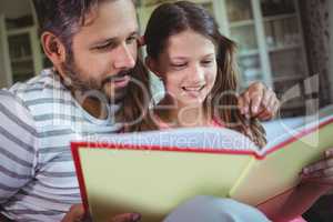 Smiling father and daughter looking at photo album in living room