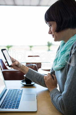 Woman using mobile phone with laptop on table