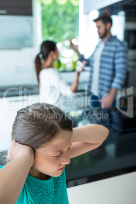 Sad girl covering her ears while parents arguing in background