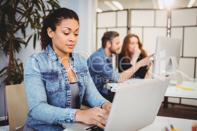 Creative businesswoman using laptop at desk against coworkers