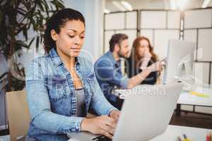 Creative businesswoman using laptop at desk against coworkers