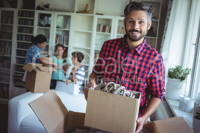 Portrait of smiling man holding a cartons while family standing in background