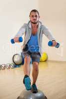 Man exercising with dumbbells on bosuball