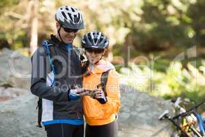 Biker couple using mobile phone in forest