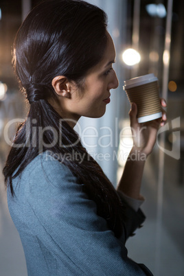 Businesswoman holding disposable coffee cup looking out of window