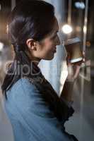 Businesswoman holding disposable coffee cup looking out of window