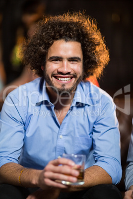 Smiling man holding glass of whisky in bar