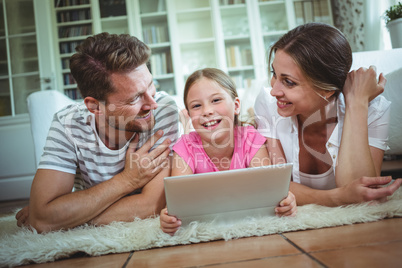 Parents and daughter lying on rug and using digital tablet