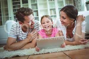 Parents and daughter lying on rug and using digital tablet