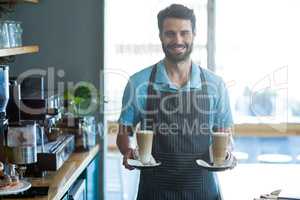Smiling waiter holding cup of cold coffee at counter in cafe