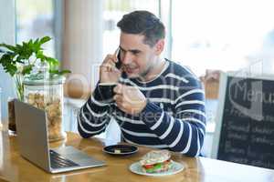 Smiling man talking on mobile phone while having coffee