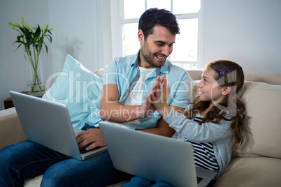 Father and daughter giving high five while using laptop in the living room Father and daughter giving high five while using laptop in the living room