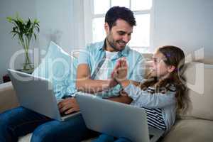 Father and daughter giving high five while using laptop in the living room