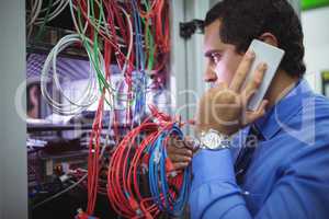 Technician talking on mobile phone while checking cables