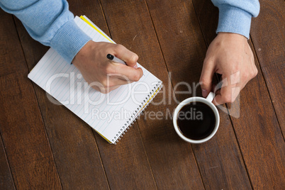 Man holding a cup of coffee and writing on notepad