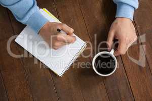 Man holding a cup of coffee and writing on notepad
