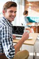 Portrait of smiling man holding coffee cup and using laptop