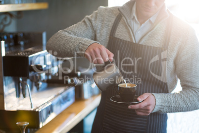 Waiter making cup of coffee at counter in cafe