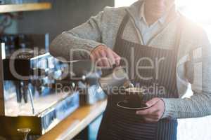 Waiter making cup of coffee at counter in cafe