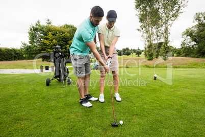 Male instructor assisting woman in learning golf