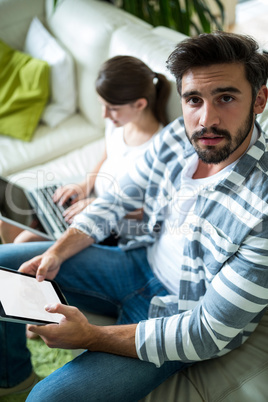 Father looking at camera while daughter using laptop in the living room