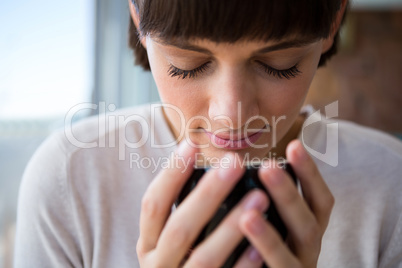 Woman smelling her cup of coffee with her eyes closed