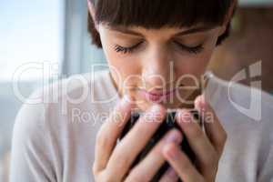 Woman smelling her cup of coffee with her eyes closed