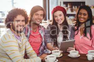 Group of friends using digital tablet while having cup of coffee