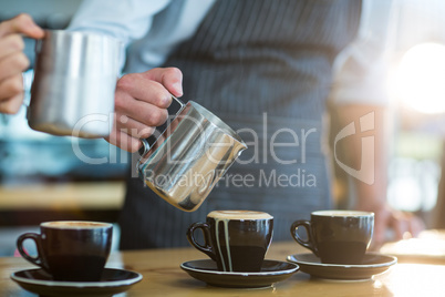 Waiter making cup of coffee at counter in cafe
