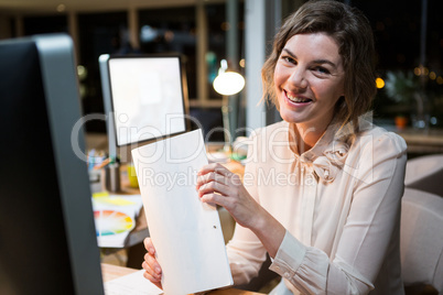 Portrait of businesswoman holding document at her desk