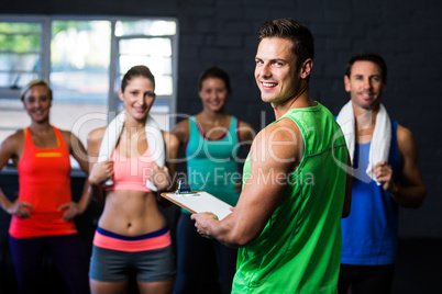 Portrait of cheerful fitness instructor with people in gym