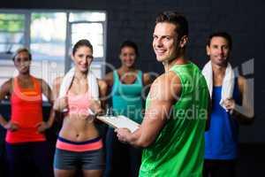 Portrait of cheerful fitness instructor with people in gym