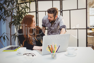 Happy colleagues dicussing while using laptop at creative office